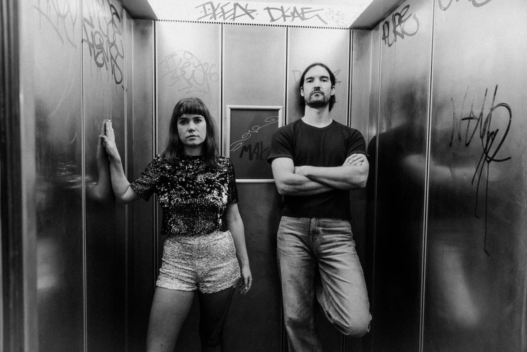 Black and white promo portrait of musical duo Party Dozen posing inside a graffiti-tagged elevator.